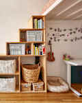 room with wood floor, wood bookcase/shelves with books, storage baskets, white walls, white beamed ceiling, white desk table against wall, more wood lower shelving with TV, plant in foreground