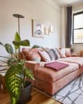 living room with wood floors, peach/pink velvet sofa, plants, large windows, wood shelves, white walls and white beamed ceiling