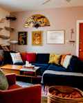 living room with navy blue velvet sofa, red and gold throw pillows, rust colored velvet accent chair, large gold/floral fan over sofa as art, cat ladders and sling beds going up the wall, floor to ceiling rust curtains, rust/terracotta colored door