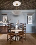 Dining room with wood floor, jute rug, dark wood sideboards, open shelving, blue-gray walls, chandelier and wallpapered ceiling.