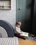 Toddler holding a book on wood floor in wallpapered playroom