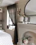 Floral bedspread on uphostered frame in neutral bedroom with mirror above fireplace