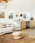 living, dining, and kitchen area with wood floors, wood kitchen cabinets, white stove, white dining table with black chairs, straw pendant light, pale neutral sofa with cane table, sisal or jute rug, straw pillows