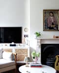Vintage painted portrait mounted above fireplace in living room with mix match vintage arm chairs and caned white framed media console.