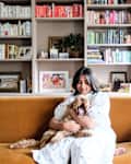 Dweller hugging dog on ochre velvet sofa in book filled living room.
