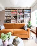 Ochre velvet sofa in book filled living room with vintage painted portrait mounted above wooden side table.