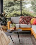 Grey outdoor sectional topped with blankets and decorative pillow in enclosed patio.