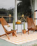 Teak outdoor chairs on top of yellow and white rug  on patio.