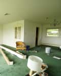 White painted room with large windows with a green carpet before renovation.