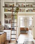 Built in library bookcase arches over threshold of living room and bedroom in light filled apartment.