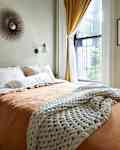 Natural light-filled bedroom with orange and white bedding in a neutral painted room.