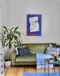 A white living room blue piece of art above a green couch and colorful rugs.