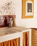 Bathroom sink with a red tiled backsplash, decorative vases, a painting, and a brown metal chair nearby.