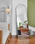 A lounge chair next to a large mirror  in a living room.