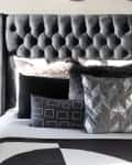 Bedroom with lots of black, white, and gray. Graphic geometric linens, throw pillows. Tufted gray headboard