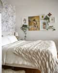 Cozy bedroom with floral wallpaper, white bedding, and framed art on the wall, accented by green plants.