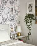 Bedroom with floral wallpaper, gold lamp on glass nightstand, and hanging plant.