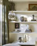 Bookshelf with decorative vases, sculptures, framed art, and books, next to a window with green curtains.