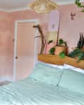 Bedroom with peach/pink walls, plants, a garment rack with colorful clothes