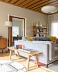 Mid-century modern living room with gray sofa, colorful cushions, wooden coffee table, abstract art, and brick fireplace.