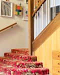 Staircase with red floral carpet, wooden dresser, potted plant, and decorative swan in a mid-century modern interior.