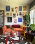 gallery wall, graphic art, orange fabric couch, curved couch, cow print rug, beads in door frame, plants, yellow tri leg bubble stool, flowers, deep purple fabric bench, red leg coffee table with glass top, disco ball, wood floors