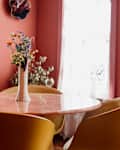Pink marble table surrounded by yellow dining chairs in pink hued dining room.