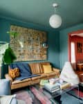 Quilt mounted above brown leather sofa in blue-green painted living room with globe pendant light and colorful rug on floor.