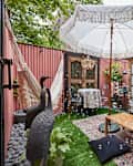 Patio with pink walls, fake grass, wood table with large white umbrella, wood and glass french doors, an off white hammock, bird statues, plants