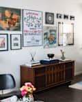 Eclectic home office with art wall gallery above wooden credenza. Potted plant sits in vintage wooden desk.