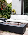 Fire pit as focal point in outdoor seating area with black wrought iron outdoor sofa and chair topped with white cushions.
