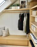 walk in closet with angled ceiling, skylight, wood slat doors, lots of wood details, hanging racks, bench with pillows