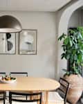 dining room with oval wood dining table, wood and black cabinet, gray walls, gray parquet floor, sisal rug, modern black pendant lamp over table, modern art on walls, large window with sheer white curtains, potted plant on floor