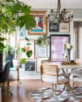 dining room with gray walls, dark bronze chandelier, marble round table with metal legs, rattan backed dining chairs with pale neutral cushions and metal legs, wood floor, round patterned area rug, gallery wall