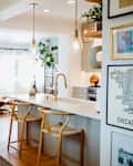 Wooden rectangular dining table with multi globe pendant hanging above. Dining table is across from kitchen bar/ sink area with two blonde wooden stools. Two hanging bulb pendants above bar area.