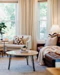 Two neutral colored arm chairs near curtain lined window in light filled living room.