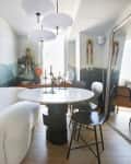 Round white and black dining table in dining room with landscape mural wall. Black chairs, and a cozy white banquette that's more like a sofa