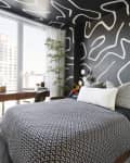 Bedroom with black walls with white bold design, bed has black and white bedding. There are large windows with a wood desk in front