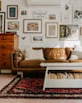 Living room with white coffee table, brown leather sofa, wooden dresser and gallery wall.