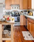 Bright kitchen with wooden cabinets, a central island holding fruit, and various kitchen appliances.