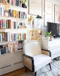 White chair next to media console in living room area of art and book filled studio apartment.