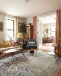 Sunny living room in Brooklyn apartment with cream colored sofa and small armchair in corner.