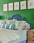 Blue velvet upholstered bed in Kelly green bedroom. Drawings of kids portraits are mounted above bed.