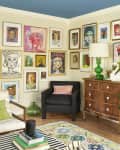 Colorful gallery wall surrounds vintage armchair and wooden dresser in living room.