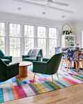 Open, sunny dining room with two seating areas. One round dining table surrounded by printed dining chairs and another round conversation area. Colorful rug lines the floor.