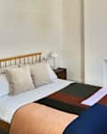 Colorful quilt on neatly made bed in all white bedroom with plastered over fireplace and floor mirror in the corner.