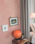 Bedroom with peach textured walls, warm lighting, white bedding, curtains around bed, large sliding glass door/window, art