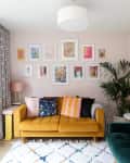 gallery wall above yellow couch, geometric pattern curtains, striped throw pillows, teal velvet couch, cuckoo clock on wall, white rug with pastel diamond pattern, large fern in corner