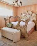 bedroom with peach sheer curtains on all the walls, a decorative carved bed with hearts and birds, and a lyrical bow chandelier