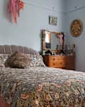 A bed with floral sheets and wooden bedroom furniture.